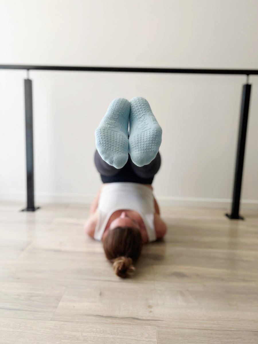 woman in plow pose with pair of powder blue tpd store grippy socks on feet showing grip soles 