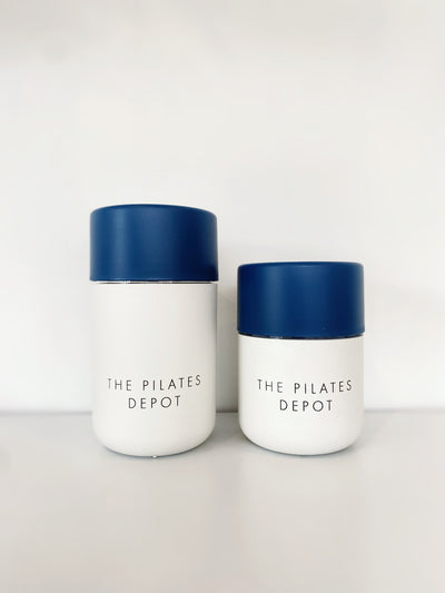 two coffee cups in white base and navy lids with the pilates depot engraved on them. One is larger than the other