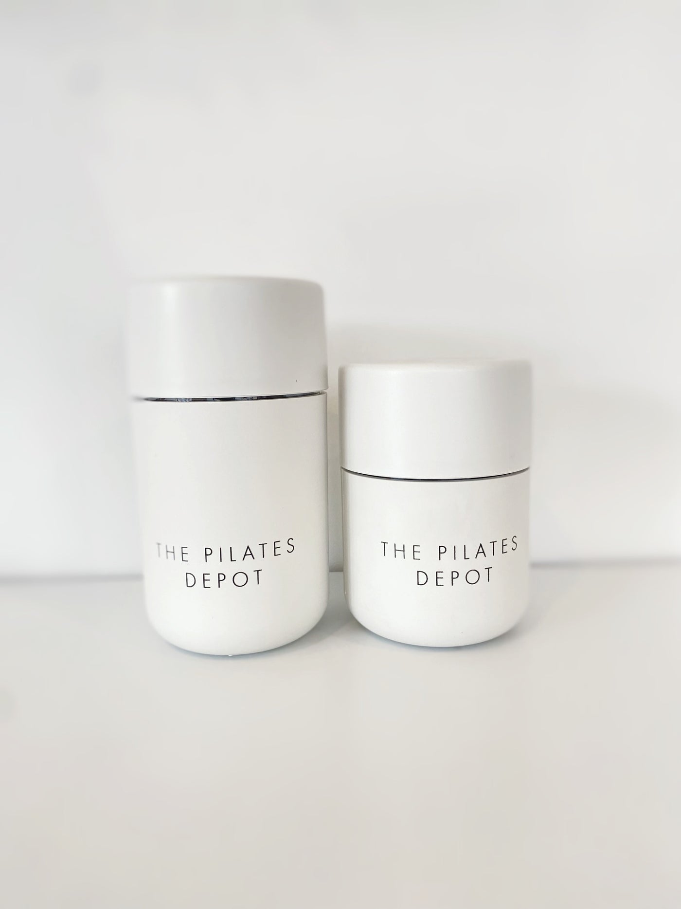two white cups with the pilates depot engraved on them. one larger than the other