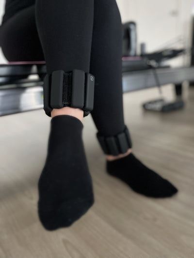 woman sitting with legs crossed wearing a pair of tpd store black ankle weights