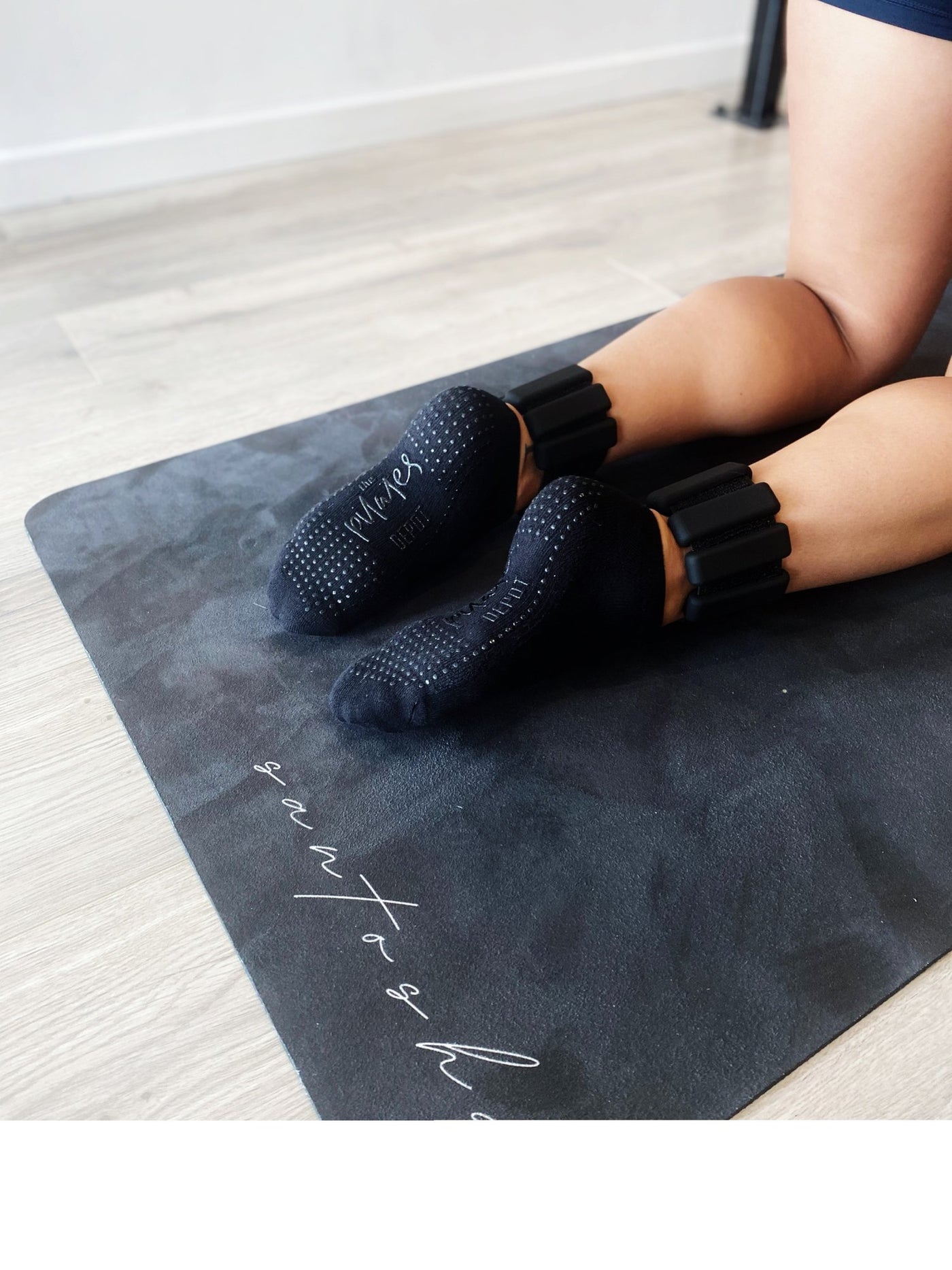 woman kneeling on snatasha mat with a pair of black tpd store ankle weights around the lower leg