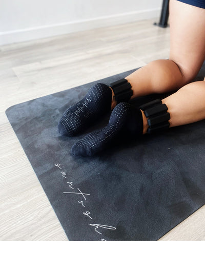 woman kneeling on snatasha mat with a pair of black tpd store ankle weights around the lower leg