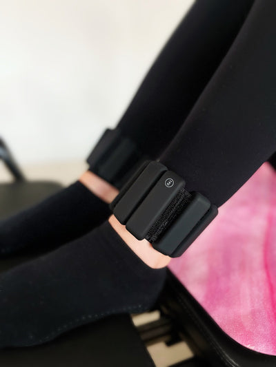pair of black tpd store ankle weights on legs bent and resting on reformer