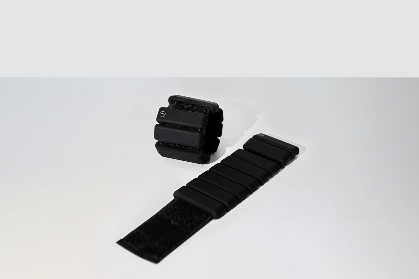 pair of tpd store black ankle weights on a white background. One unrolled and one in a ring