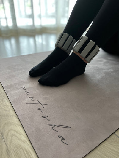 pair of feet resting on a santasha yoga mat wearing grey tpd store ankle weights.