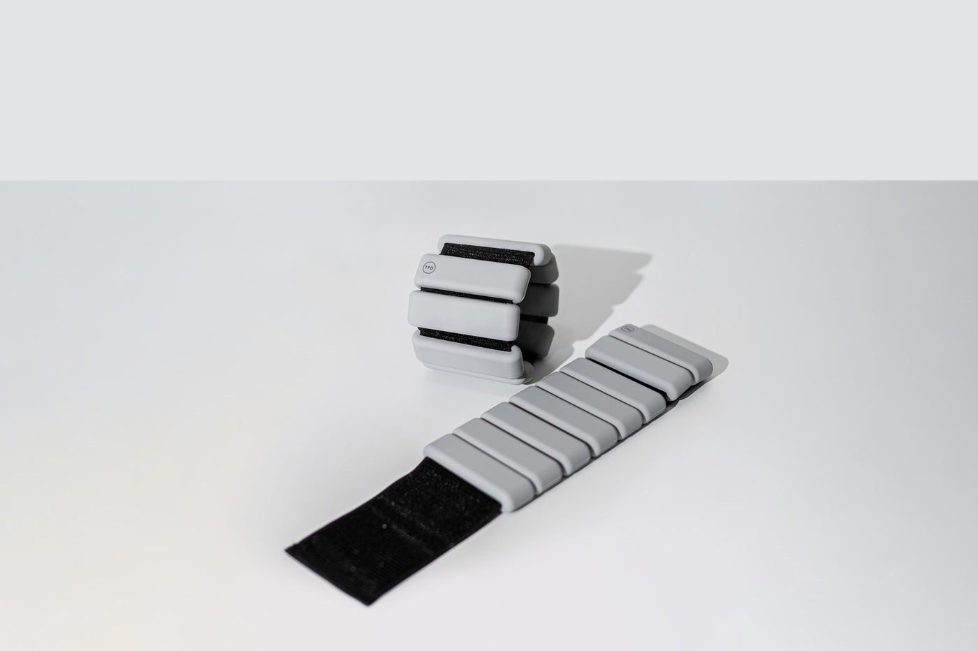pair of tpd store grey ankle weights on white background. One unrolled and one in a ring