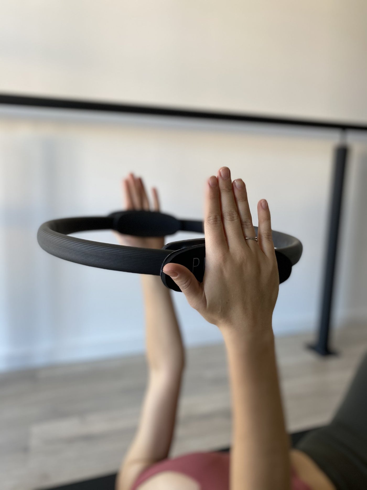 pair of hands holding a tpd store black pilates ring above her chest while lying on her back