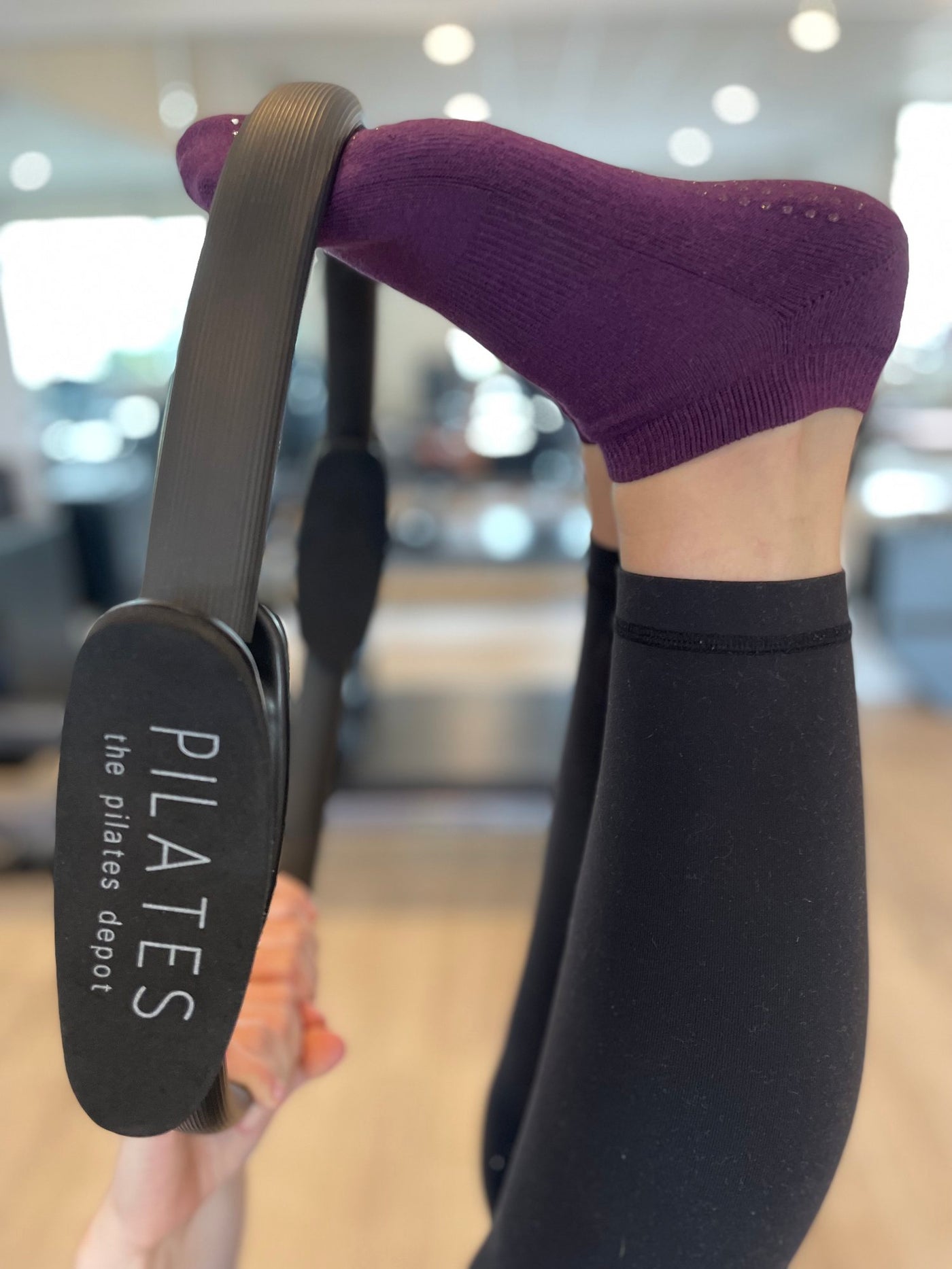 woman lying on her back with feet raised and toes inside the black tpd store pilates ring