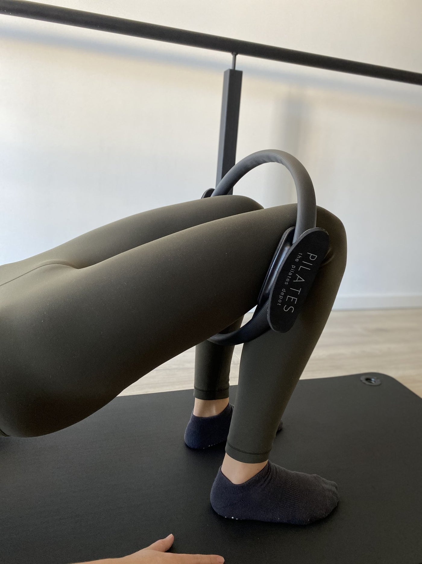 woman lying on her back in bridge position with her legs inside a black tpd store pilates ring positioned around her lower thighs