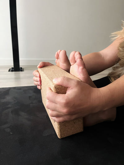 hands holding tpd cork block in forward fold pose with block beyond her feet