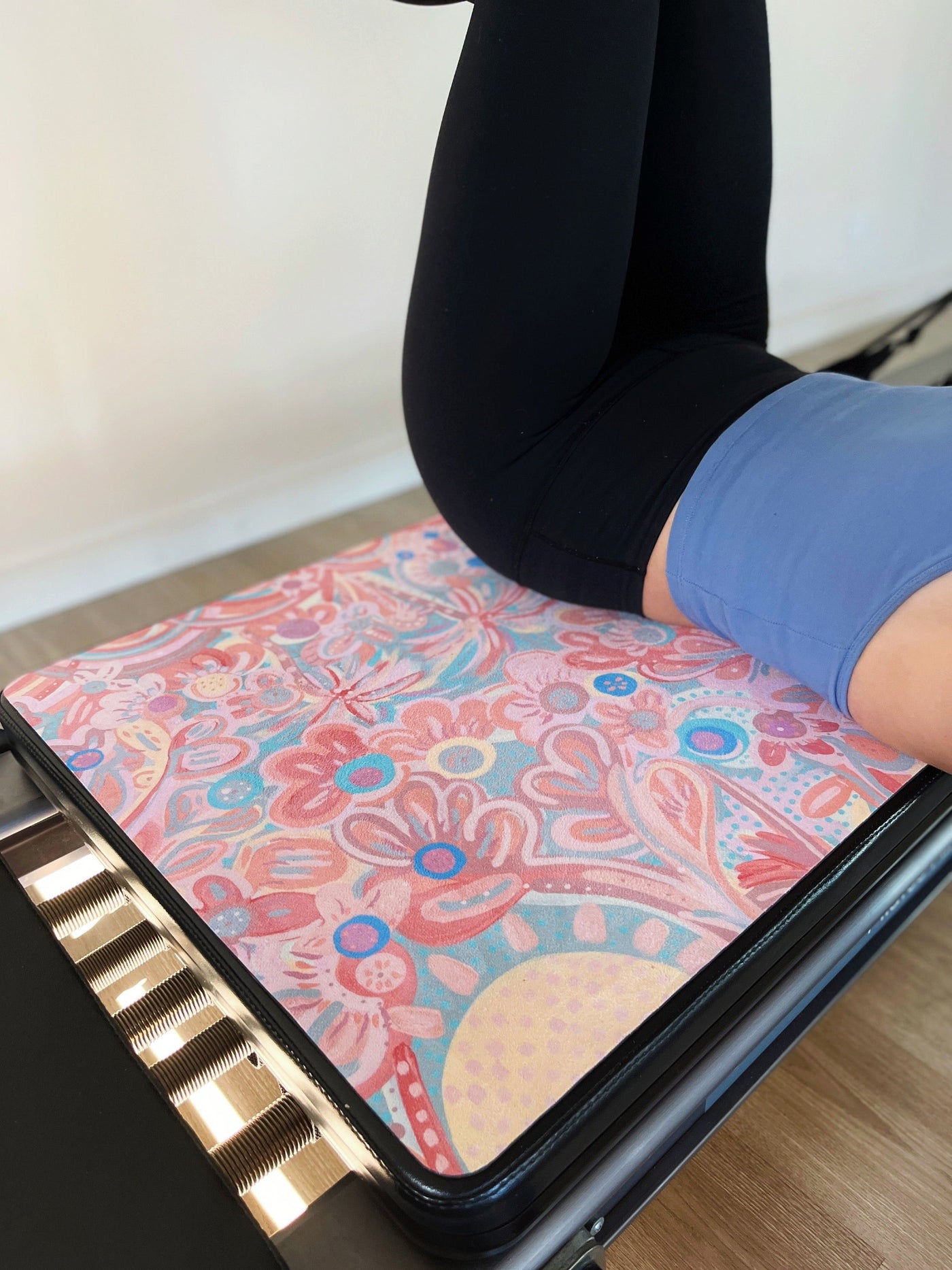 woman lying accross a pilates reformer with a TPD Store eco friendly reformer mat in You are my sunshine Aurora Art Collab print