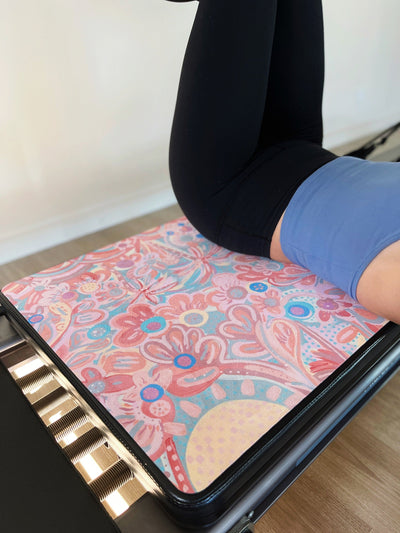 woman lying accross a pilates reformer with a TPD Store eco friendly reformer mat in You are my sunshine Aurora Art Collab print