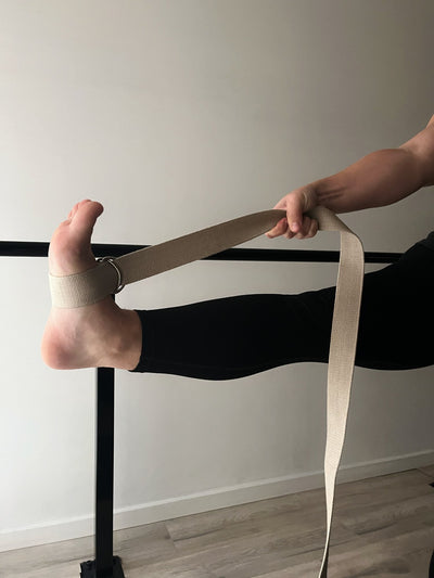 woman with tpd store organic cotton strap around her lifted leg being pulled towards hip height