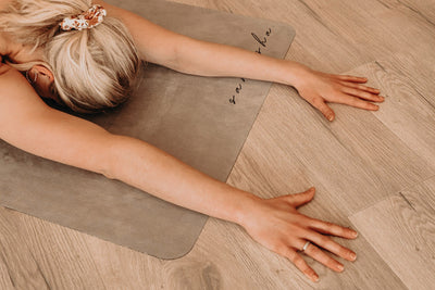 woman in childs pose with hands byond the edge of the stone coloured tpd store edo friendly yoga mat