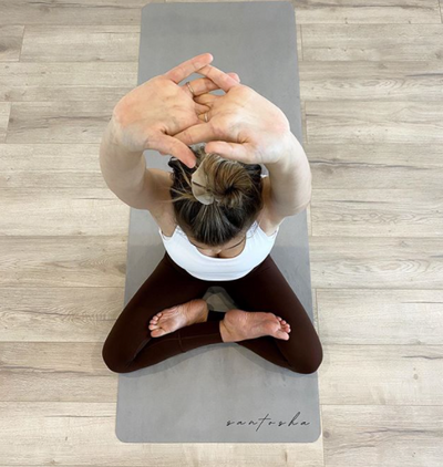 woman sitting in lotus pose with hands above head, sitting on a stone tpd store eco friendly yoga mat