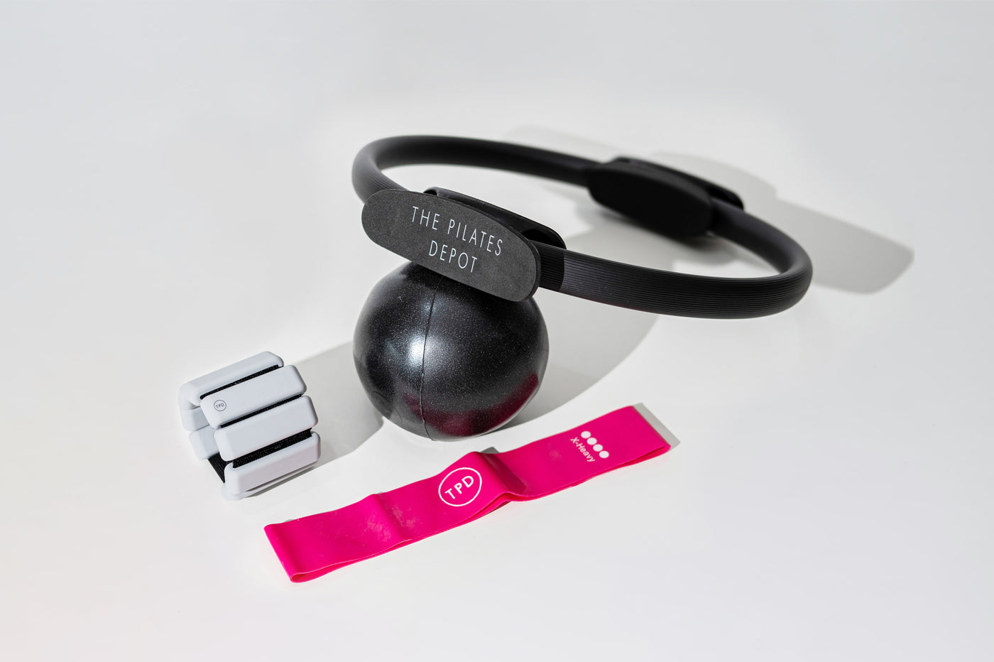 the pilates depot store black pilates ring, pink resistance band, ankle weights in grey and black chi ball in a bundle on the floor