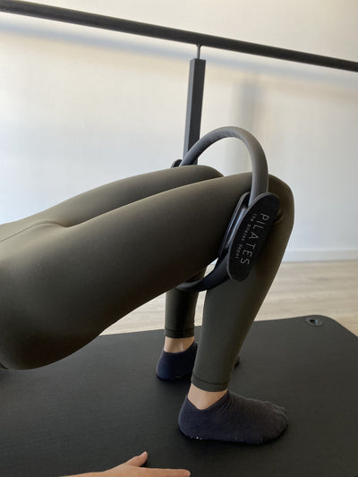 a pair of legs inside a black pilates ring with the pilates depot in white written on it