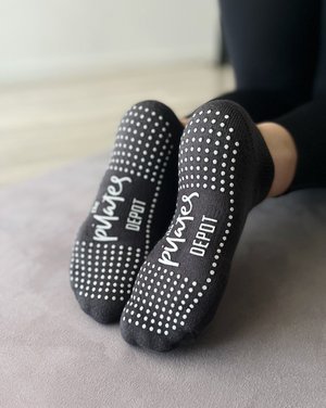 a pair of feet wearing charcoal grey low rise tpd store grippy socks with grip sole showing