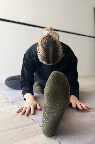 woman with one foot out in seated streach wearing tpd store grippy socks in Kahki low rise style
