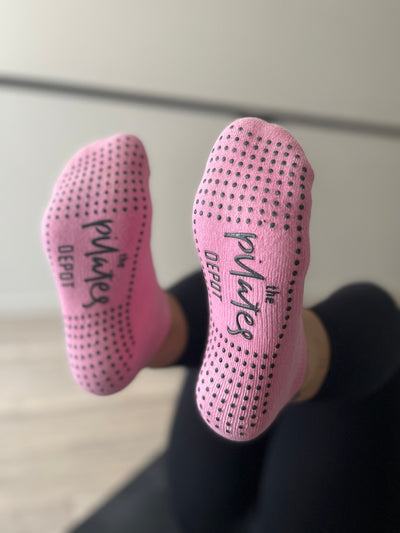 pair of feet raise wearing a pair of pink blush low rise tpd grippy socks showing grip sole